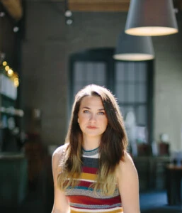 2011 grad Bethany Lackey, a young woman with long dark hair and a sleeveless striped dress, posing in front of a muted indoor backdrop