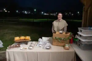 Vendor in brown dress at a table of baked goods at BRIM Christmas event outdoors