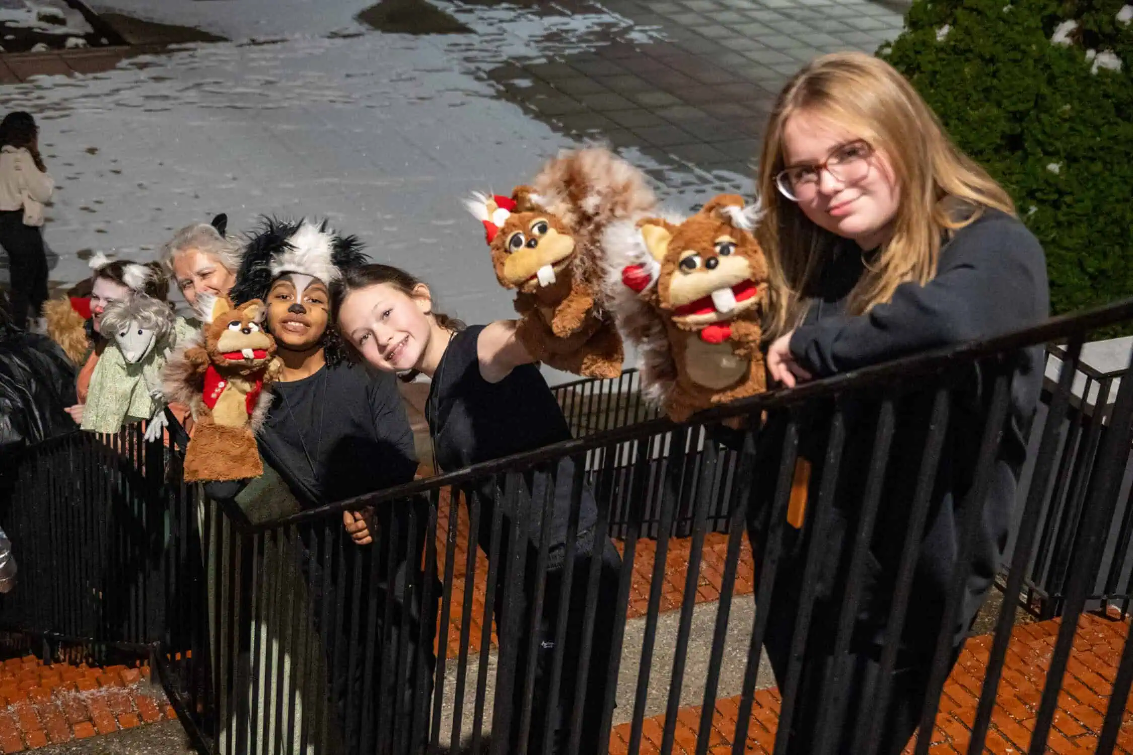 Actors of different ages along the iron railing of Schoolfield Hall steps, in Emmet Otter costumes with squirrel and possum puppets