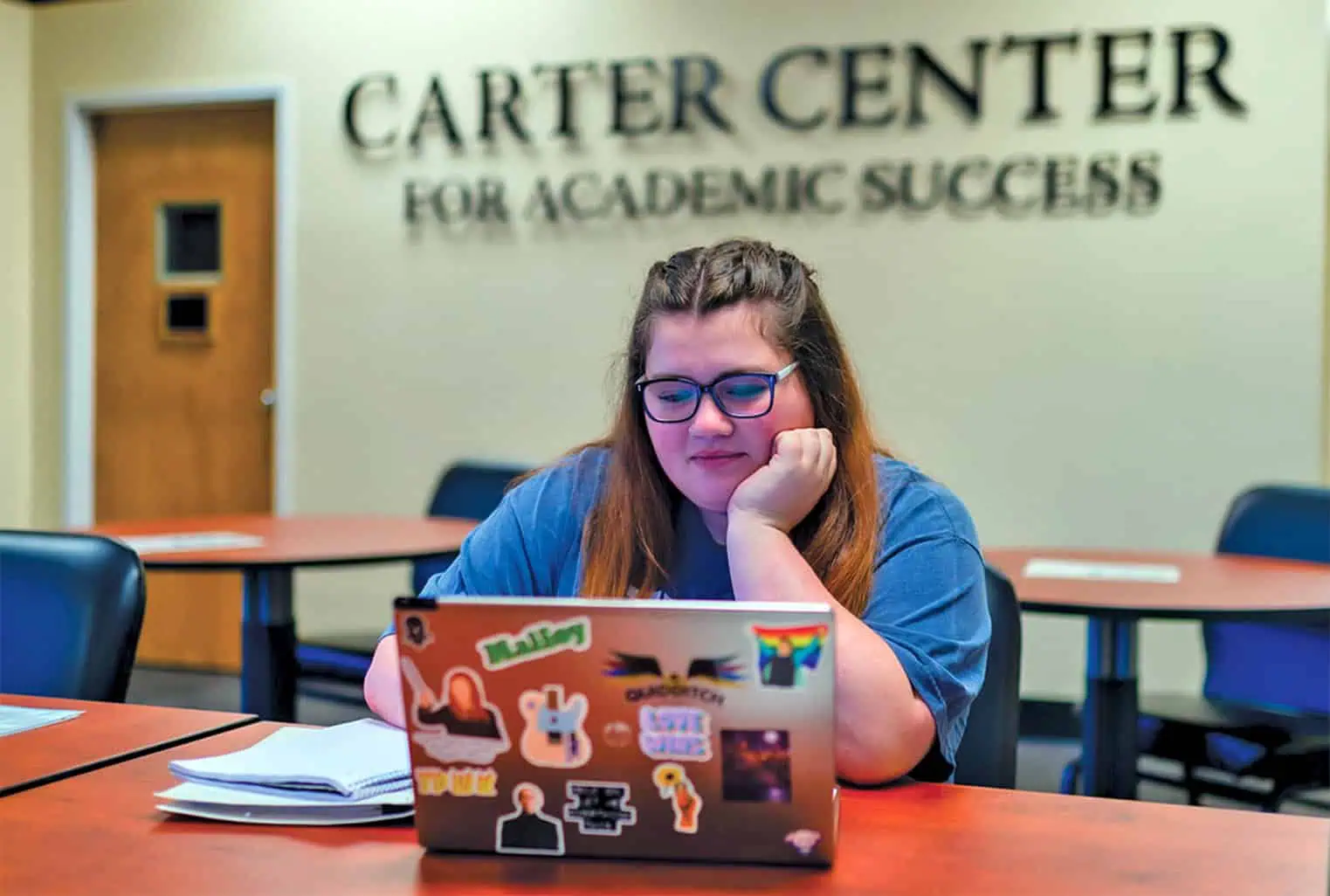 A student with an open laptop in front of her with the Carter Center sign behind her