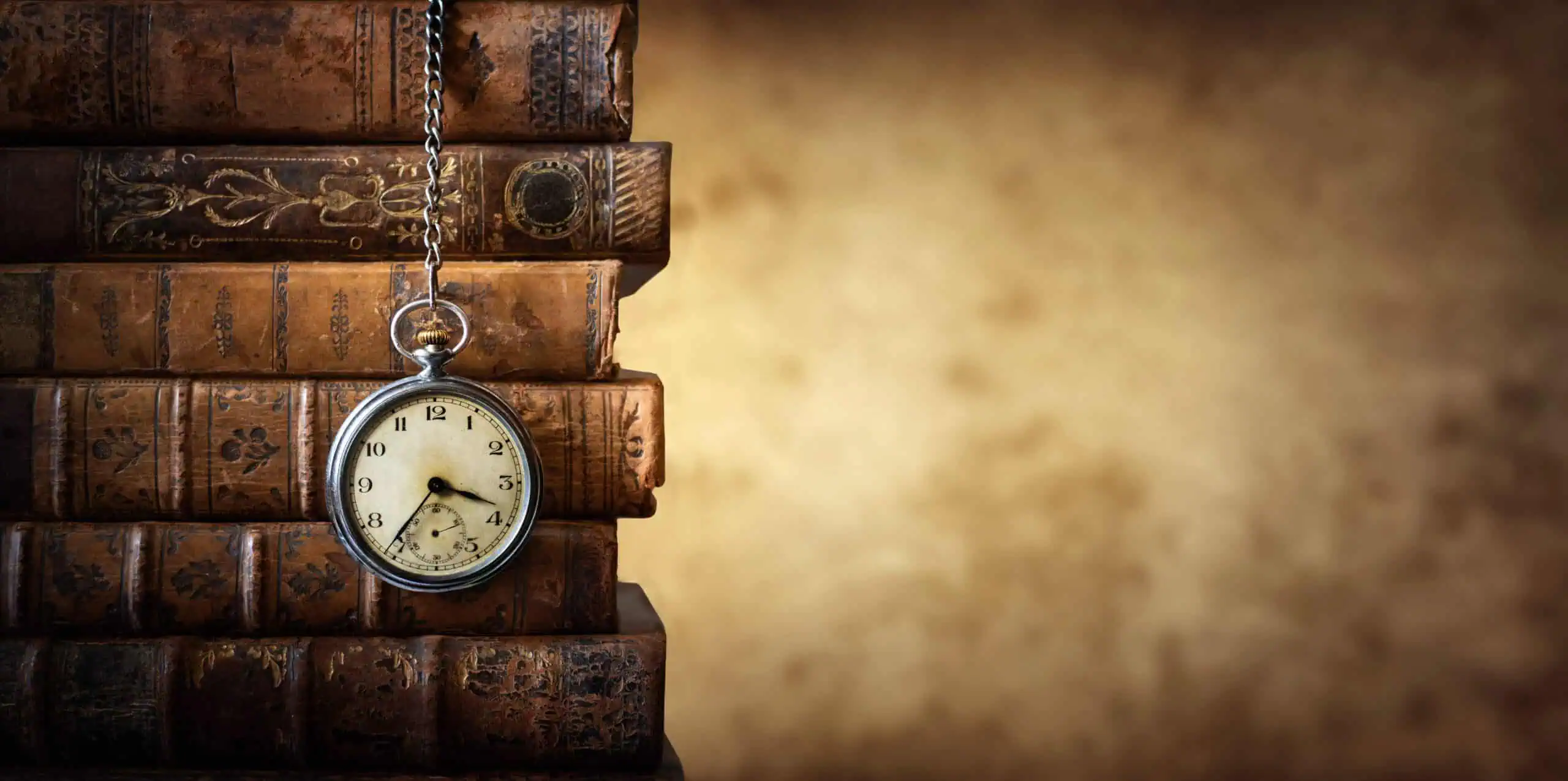 stack of books on the far left side with a watch hanging over them in front of a brown background