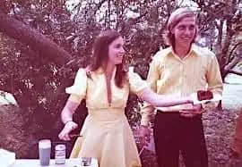 Young Carolyn Thomas and Bob Pohlad sharing wedding cake, both dressed in yellow at their outdoor wedding in 1975 