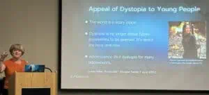 Dr. Lana Whited lecturing with slide about dystopia projected on library wall