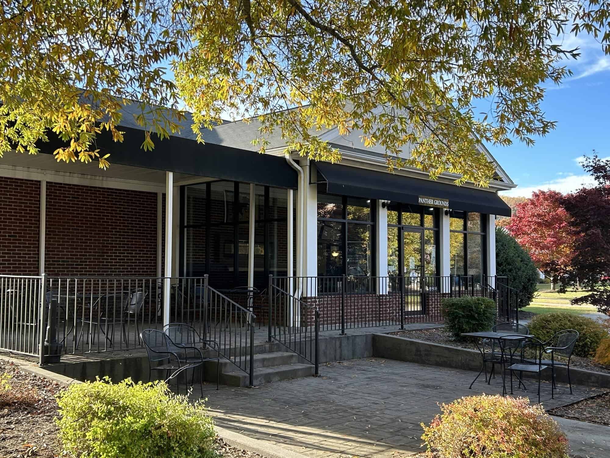 Back of Panther Grounds campus store, small brick building with white trim and large windows, with some outdoor landscaping and tree branches around it