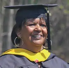 Head shot of Margaret Drakeford in black graduation cap and gown with gold collar, dark hair and big hoop earrings