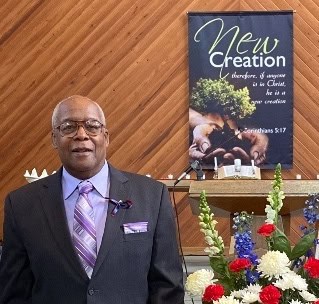 Dr. Melvin Macklin in a suit with flowers and a banner in Vaughn Chapel at Ferrum College