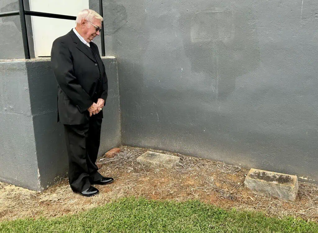 Dr. William Wray in dark suit viewing two gravestones behind Schoolfield Hall