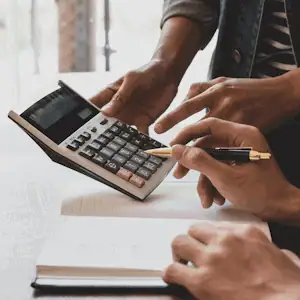 Two people focusing on a handheld calculator that one of the people is holding.