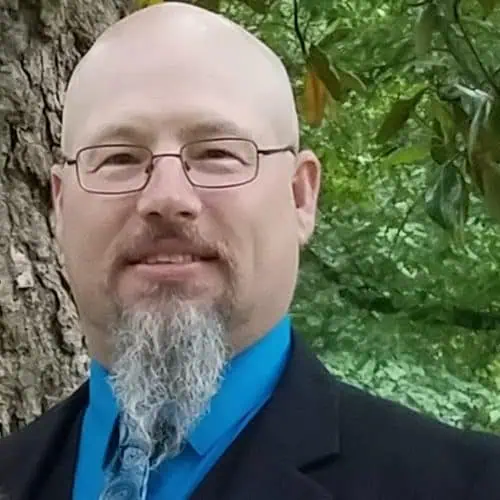 Headshot of Ferrum College professor Andy Flora wearing a black suit jacket, blue dress shirt and tie.