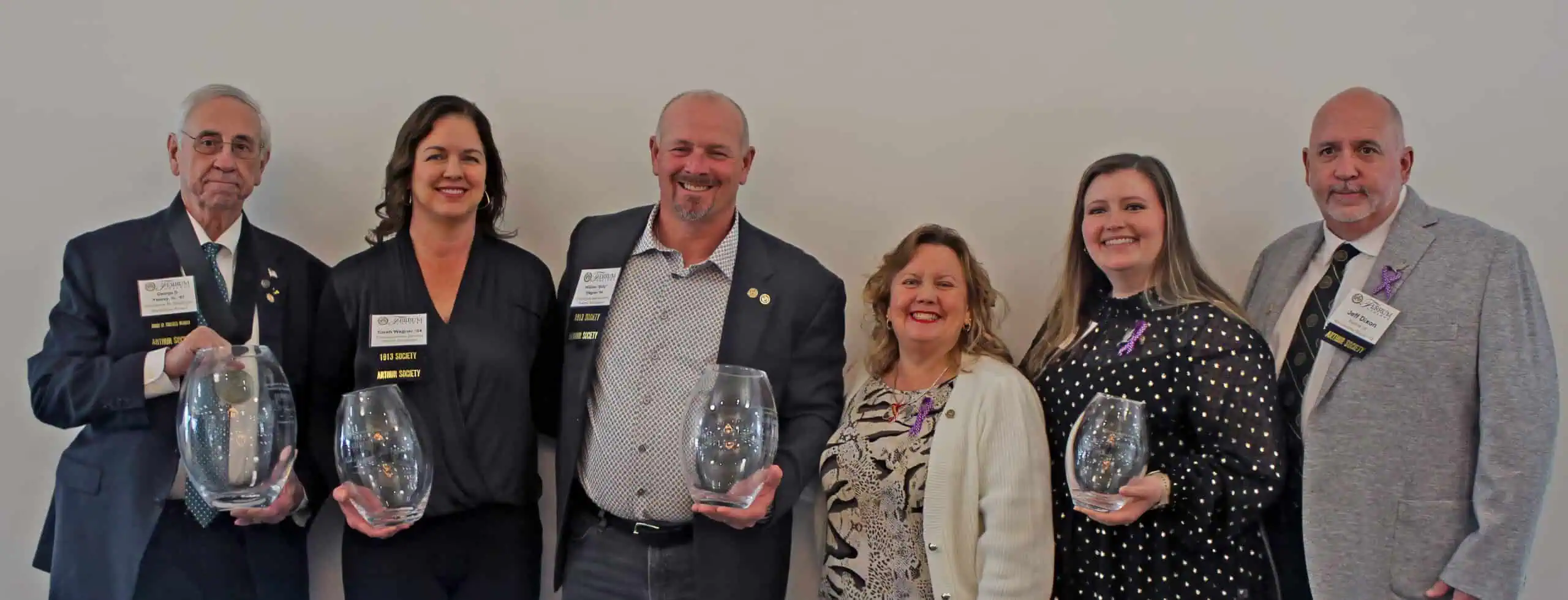 Five professionally dressed individuals standing side by side, three holding glass awards, smiling against a plain background.