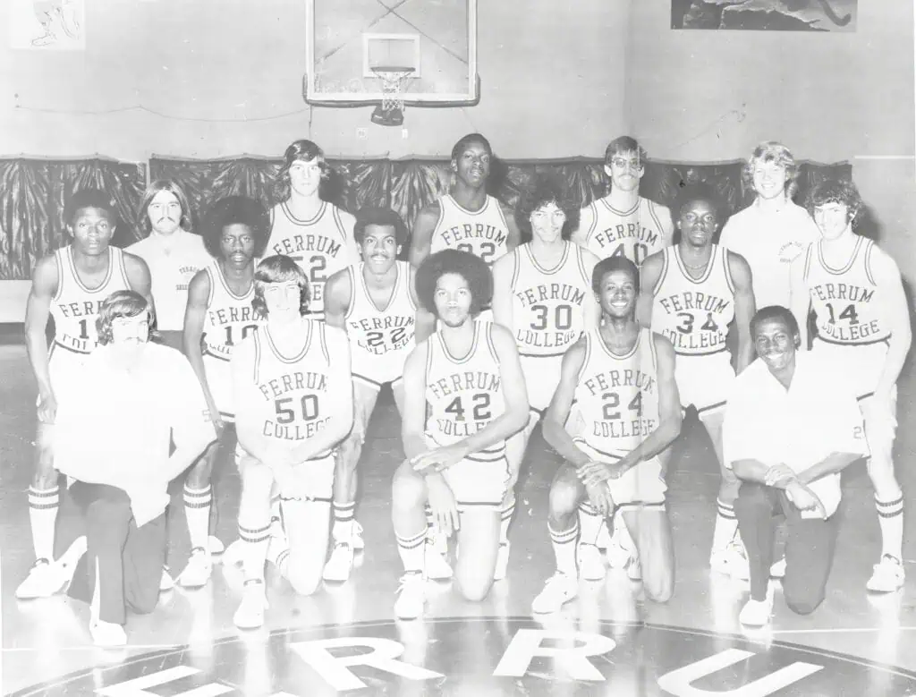 Black and white yearbook photo of 1974-75 basketball team with 16 young men posed in rows in a basketball court.