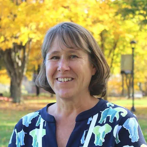 leslie holden in blue elephant shirt outside in front of trees with yellow leaves for staff photo