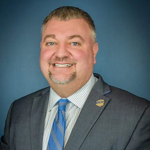 christopher parker in gray suit in front of blue background for staff photo