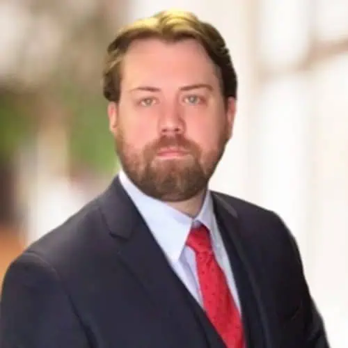 Headshot of Ferrum College professor Ryan Cooper who is wearing a dark suit, light colored shirt, and red tie