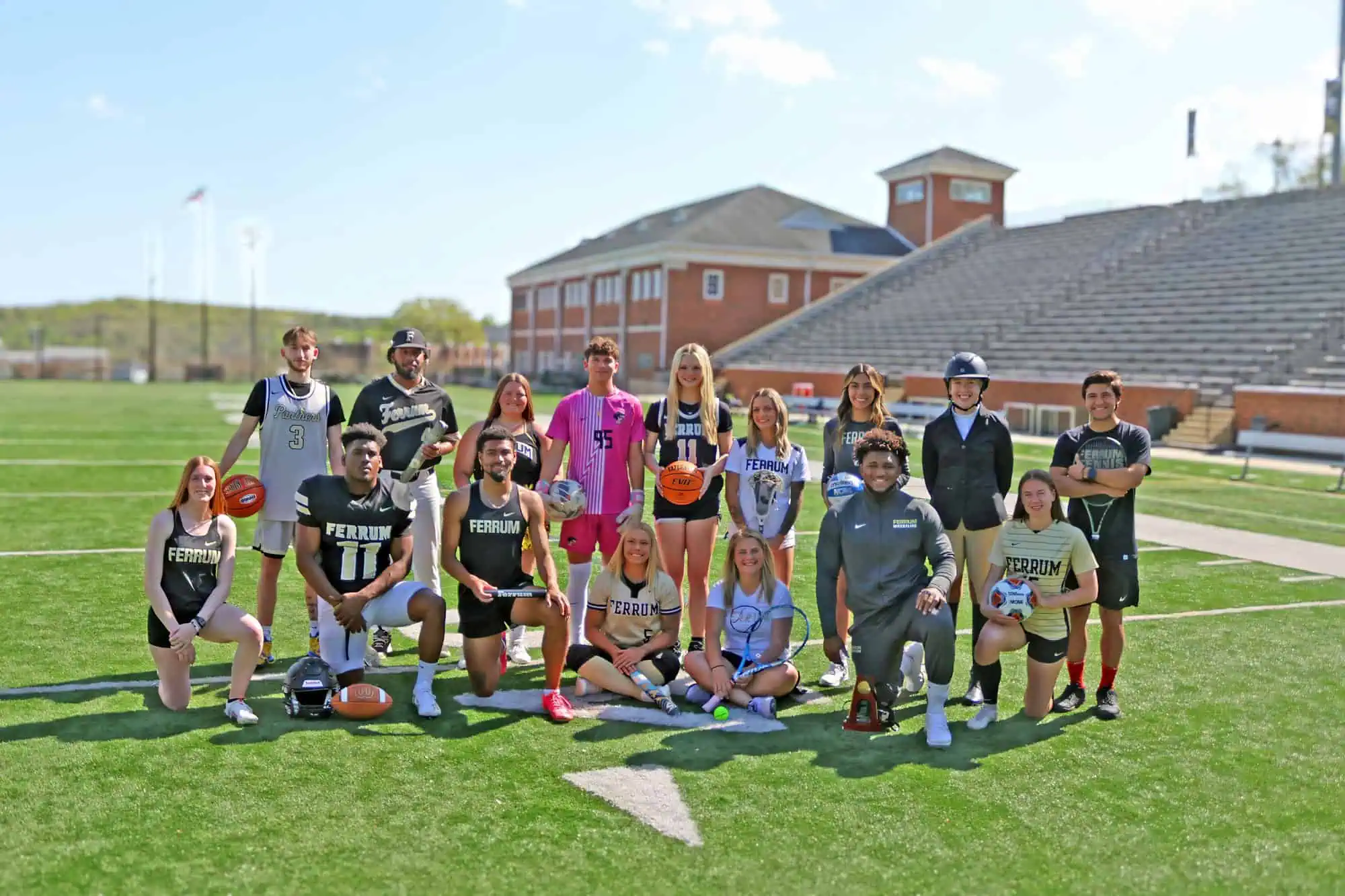 A group of Ferrum College student athletes pose on the football field in Adams Stadium with the Hank Norton Center behind them