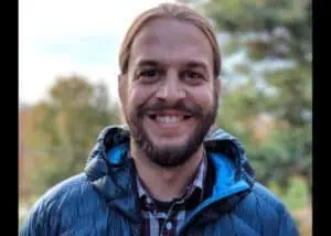 Man wearing a blue jacket is smiling brightly to the camera.